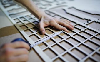 Hands of craftsman measuring plywood sheet with cut cells